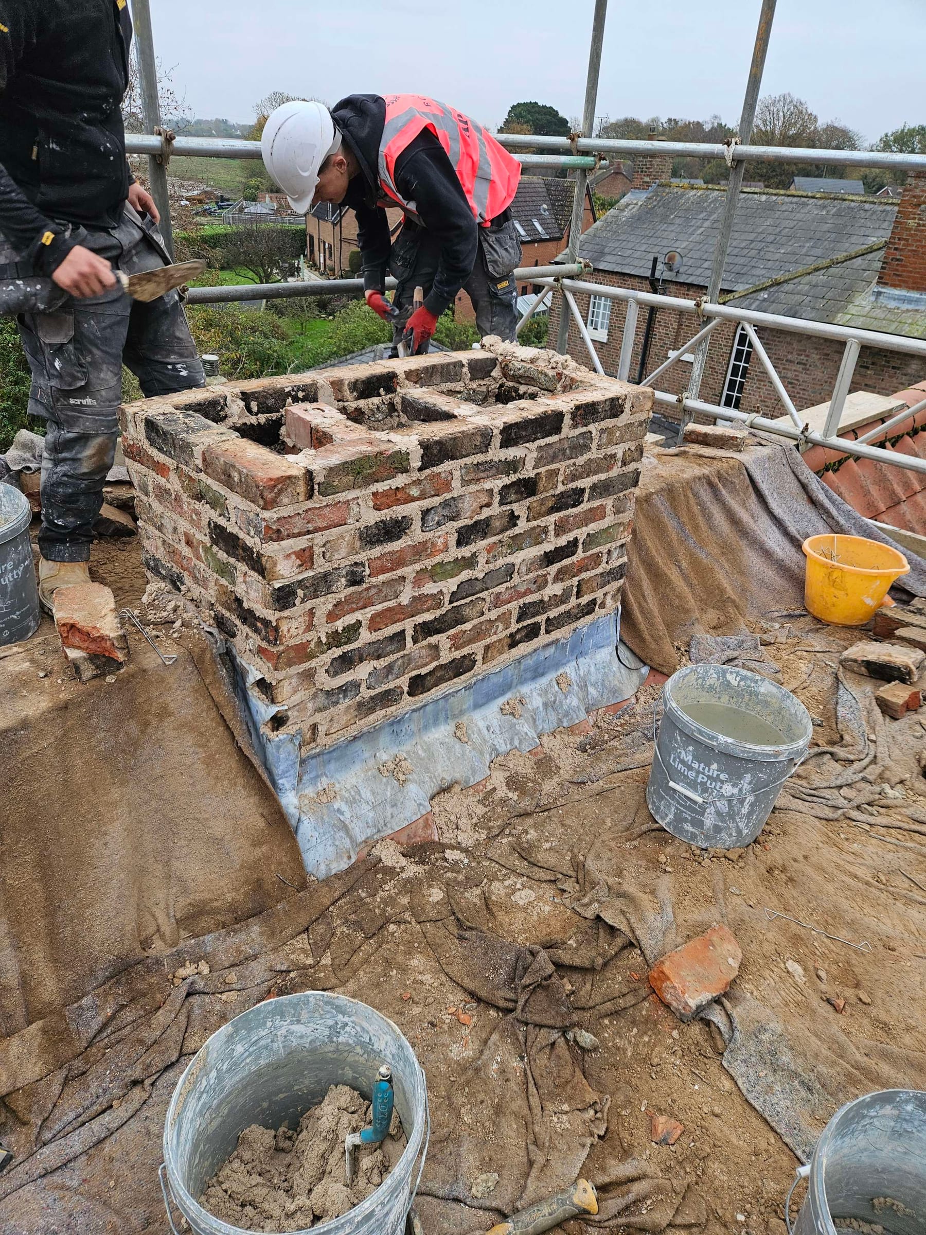 Bricklayers rebuilding a chimney stack on a roof